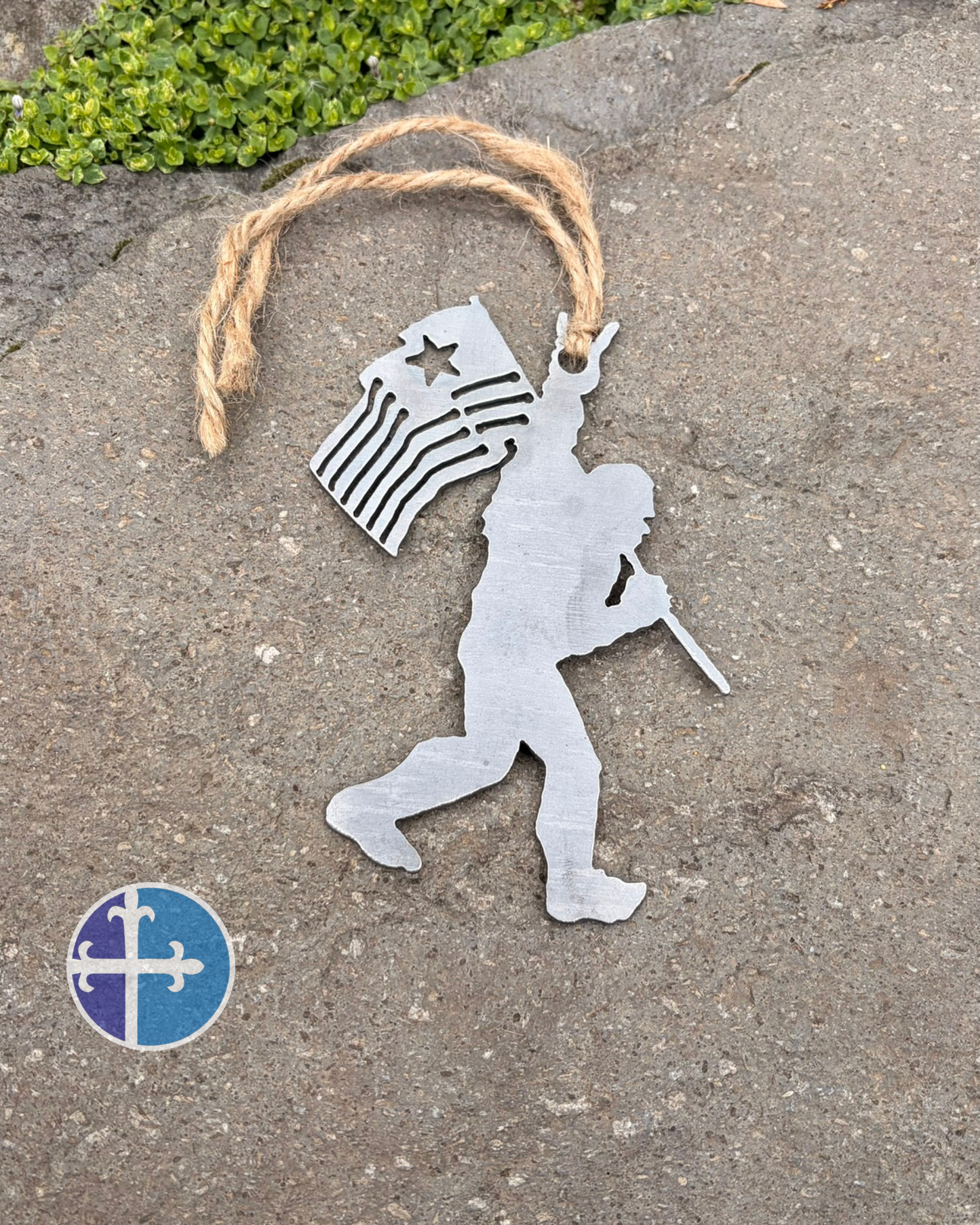 Rustic Sasquatch ornament made from raw steel with a waving American flag and rock-on gesture hanging from twine.