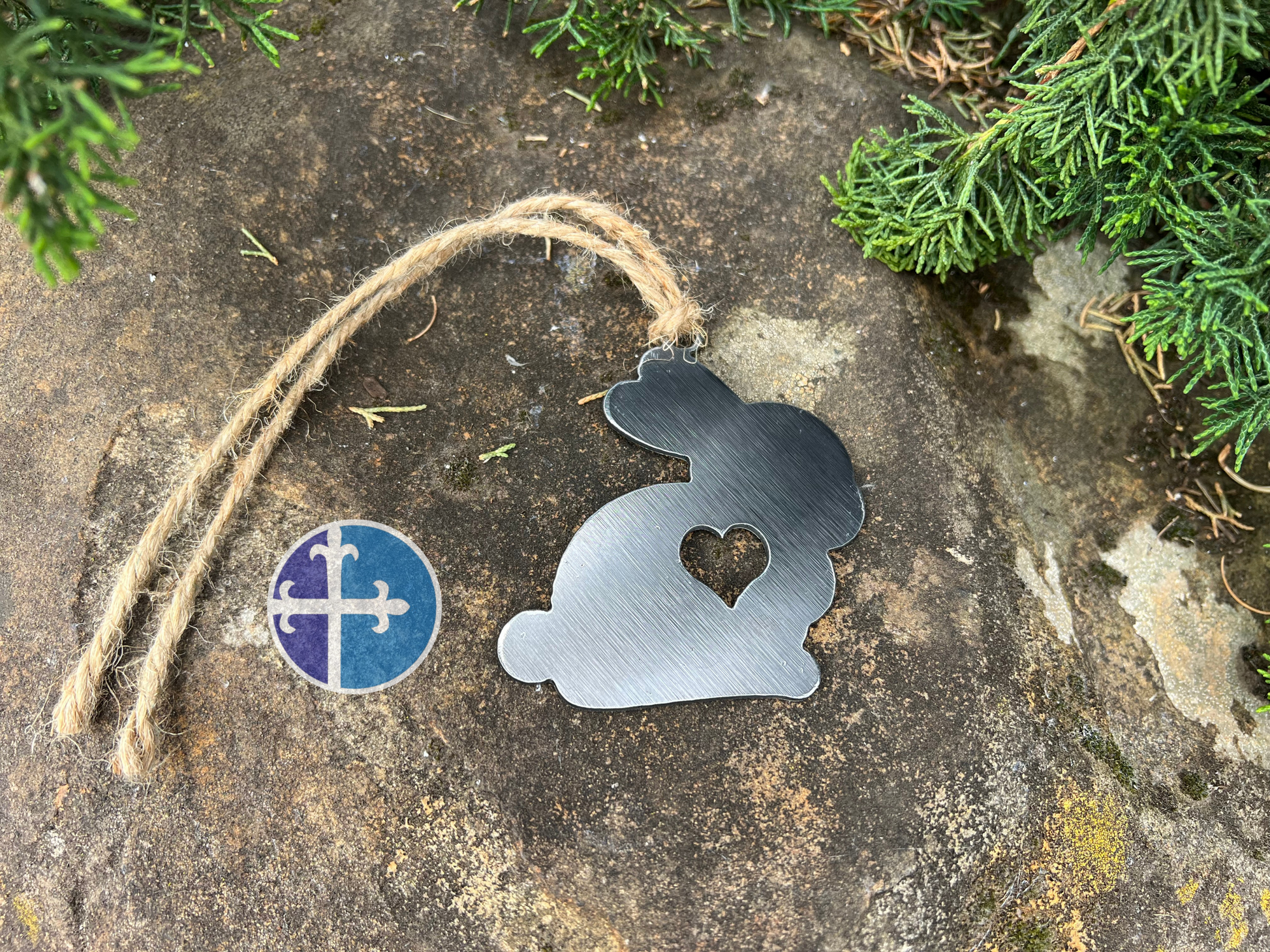 Side view of a rustic metal bunny ornament with a heart cutout, hanging on a jute string, showcasing its farmhouse style.