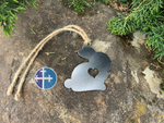 Load image into Gallery viewer, Side view of a rustic metal bunny ornament with a heart cutout, hanging on a jute string, showcasing its farmhouse style.
