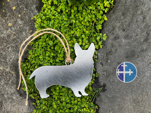 Metal Corgi silhouette ornament resting on rock with green moss.