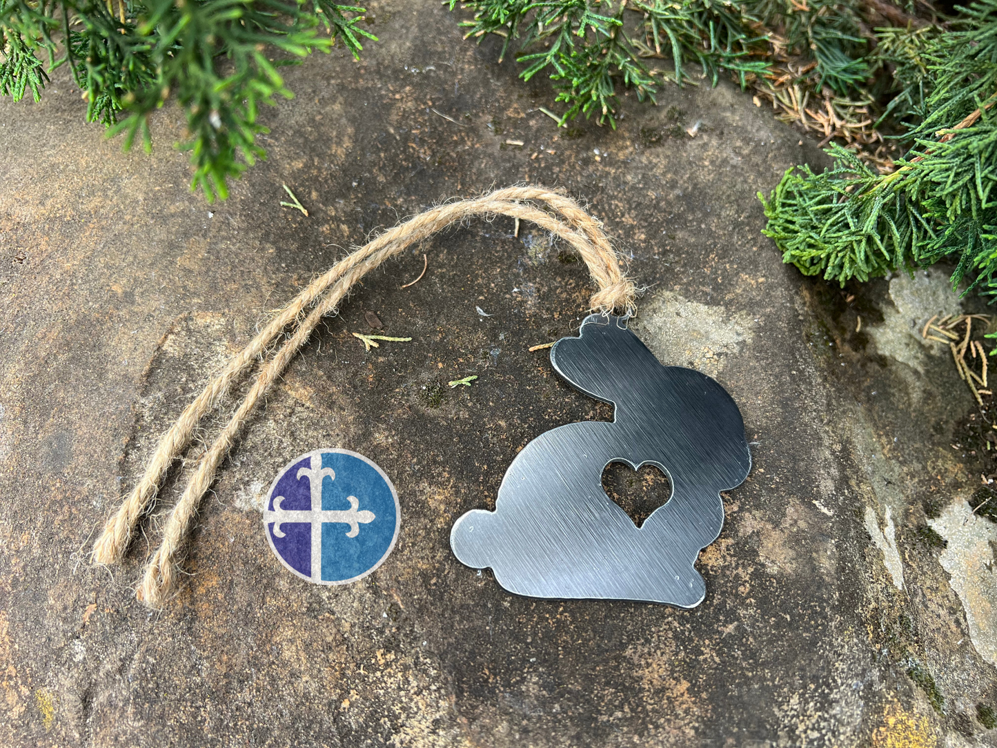 Detailed image of a brushed metal bunny ornament with a heart cutout, hanging against a natural background, featuring a jute string for easy hanging.