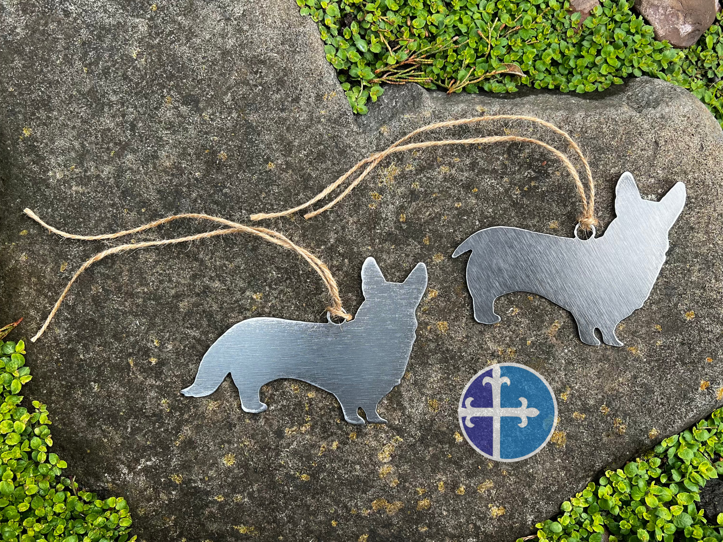 Two brushed metal Corgi ornaments side by side on natural rock surface.