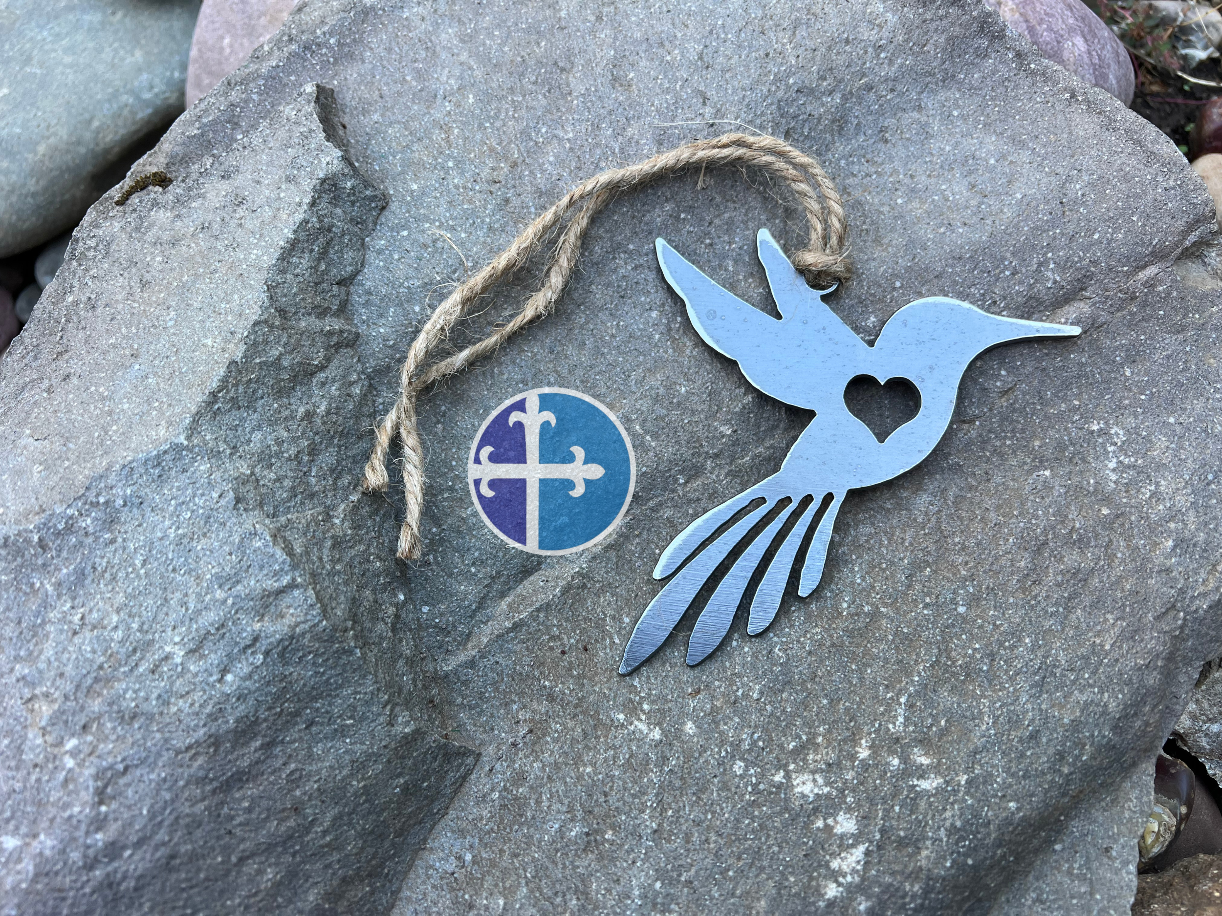 Rustic steel hummingbird decoration, laying on gray stone, showing heart detail.