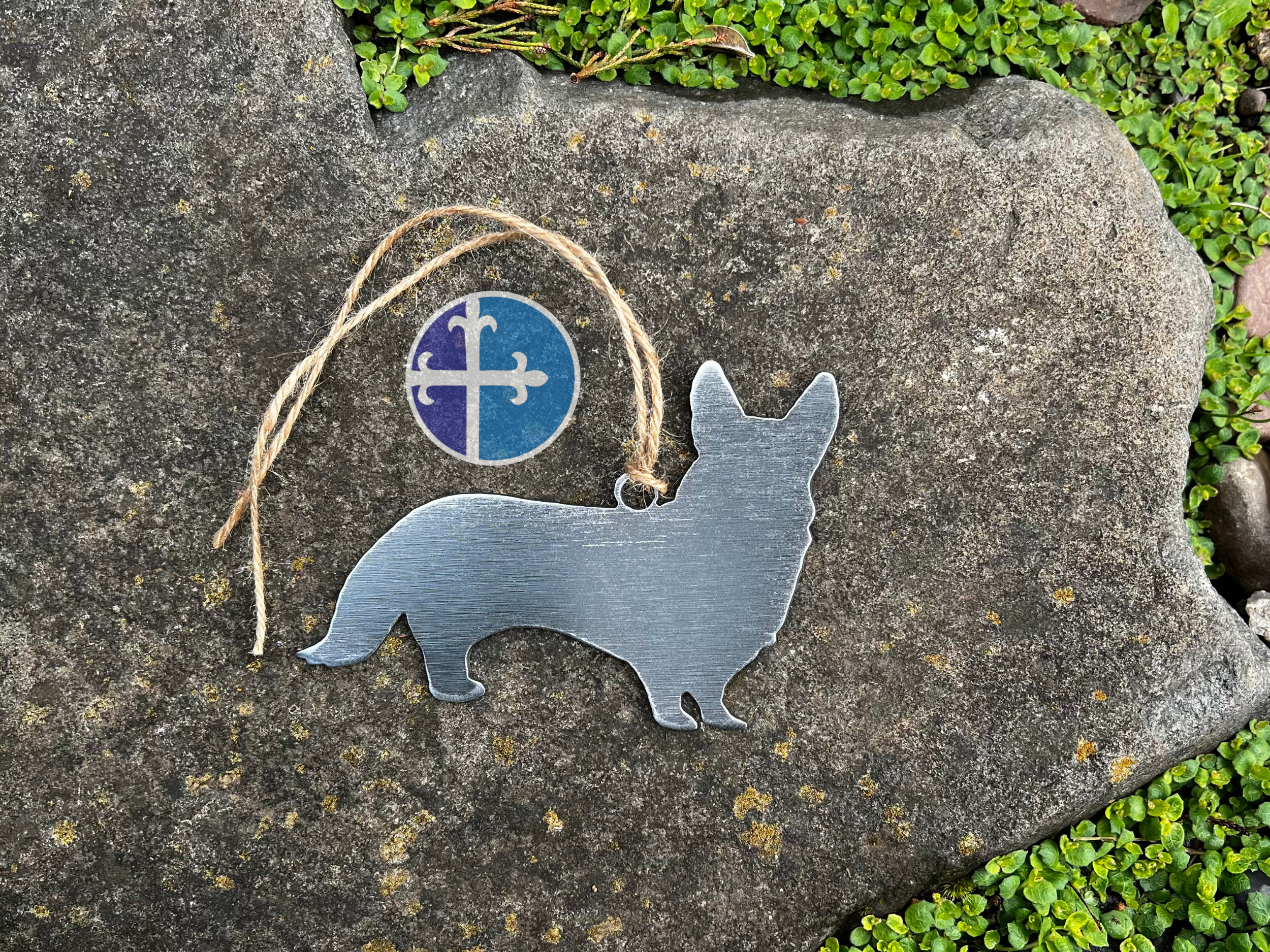 Brushed steel Corgi dog ornament with twine hanger on stone background.