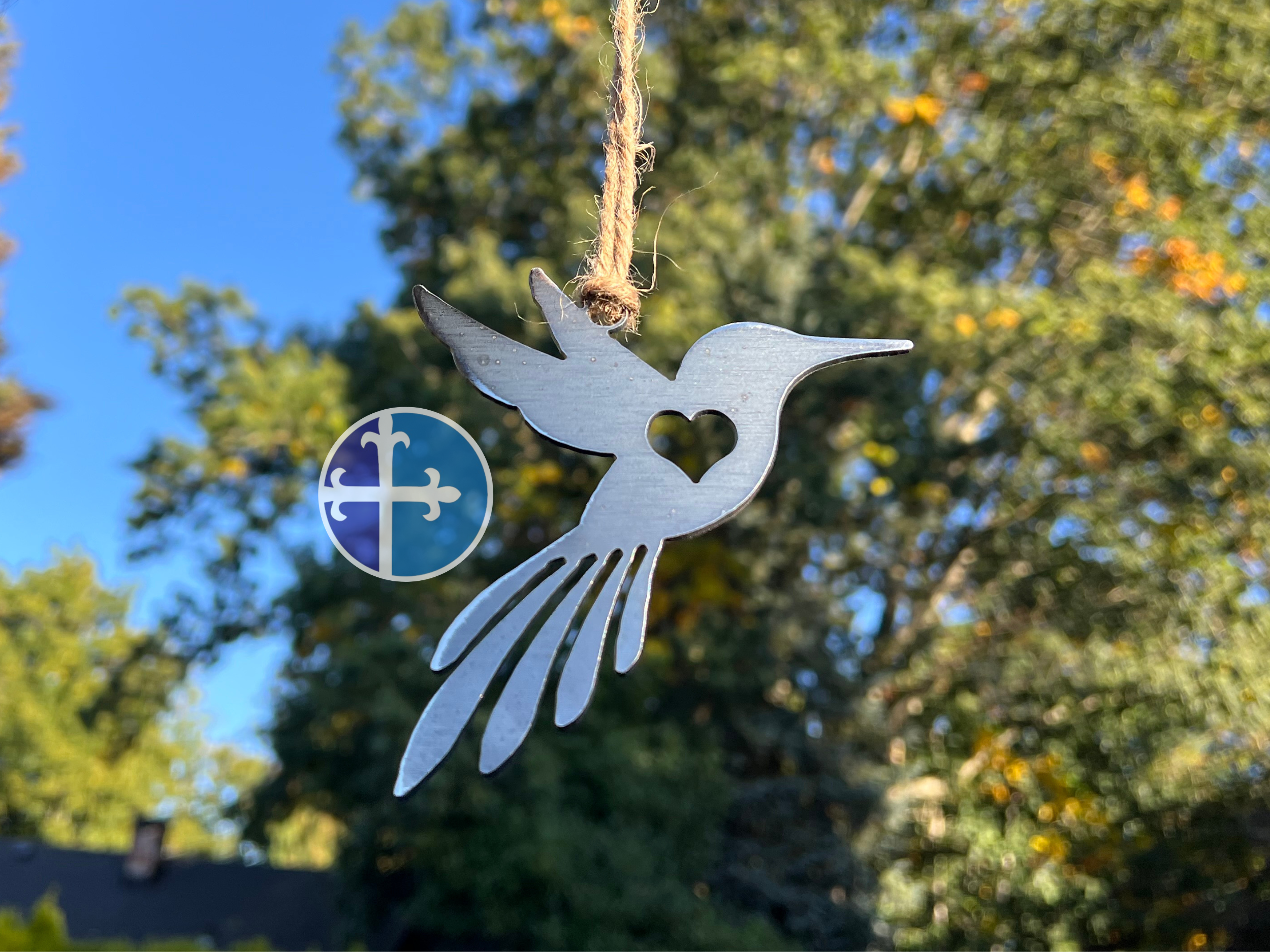 Rustic hanging hummingbird ornament, floating with blue sky and green tree background.