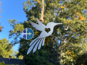 Rustic hanging hummingbird ornament, floating with blue sky and green tree background.