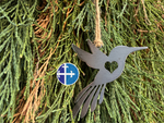 Load image into Gallery viewer, Close-up of steel hummingbird hanging ornament against cedar greenery, emphasizing rustic metal texture.
