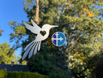 Load image into Gallery viewer, Hummingbird silhouette ornament made of durable steel, hanging from twine with a nature-filled backdrop.

