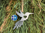 Load image into Gallery viewer, Close-up of steel hummingbird hanging ornament against cedar greenery, emphasizing rustic metal texture.
