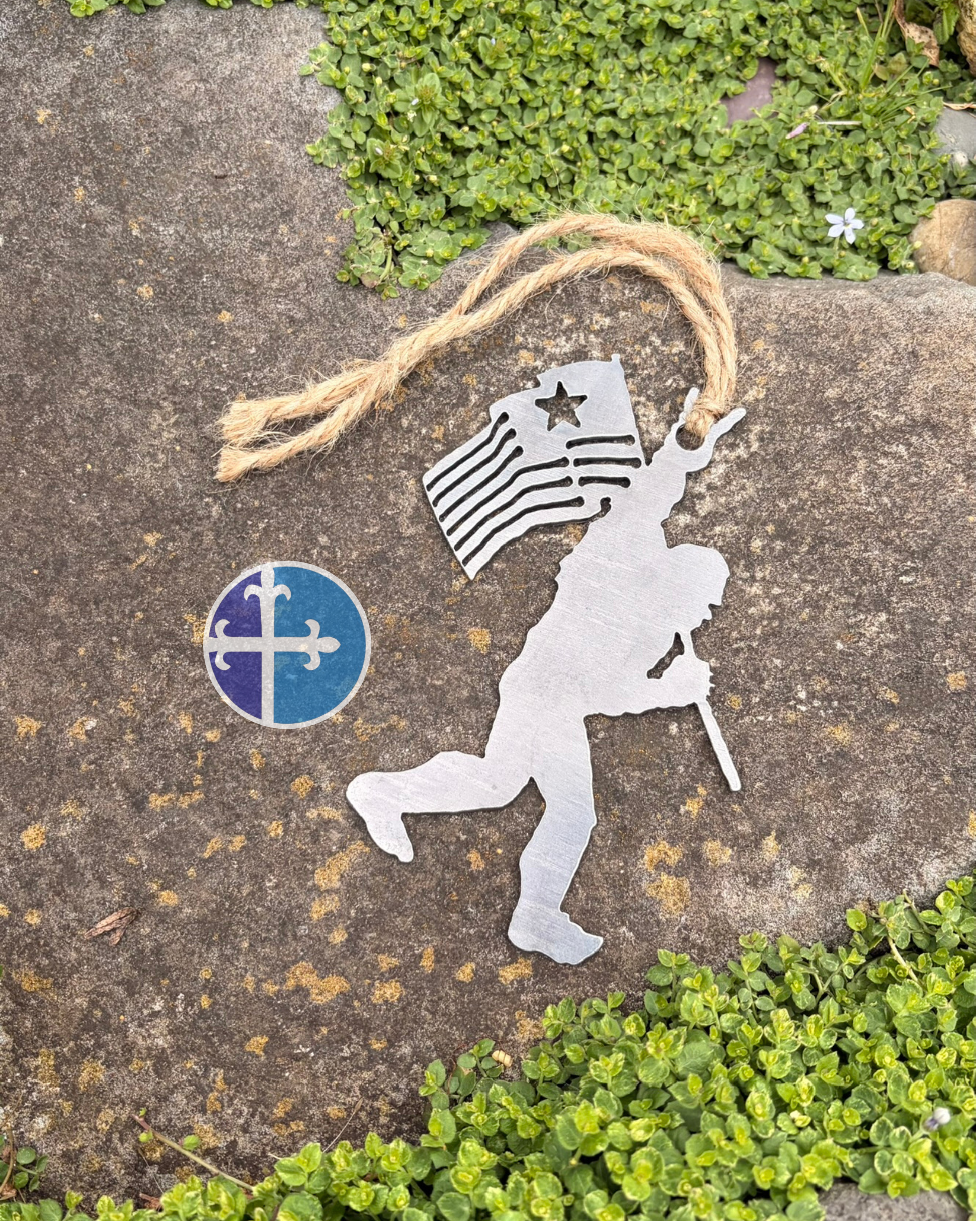 Close-up of raw steel Sasquatch ornament with American flag and raised rock-on fingers hanging from rustic jute twine.