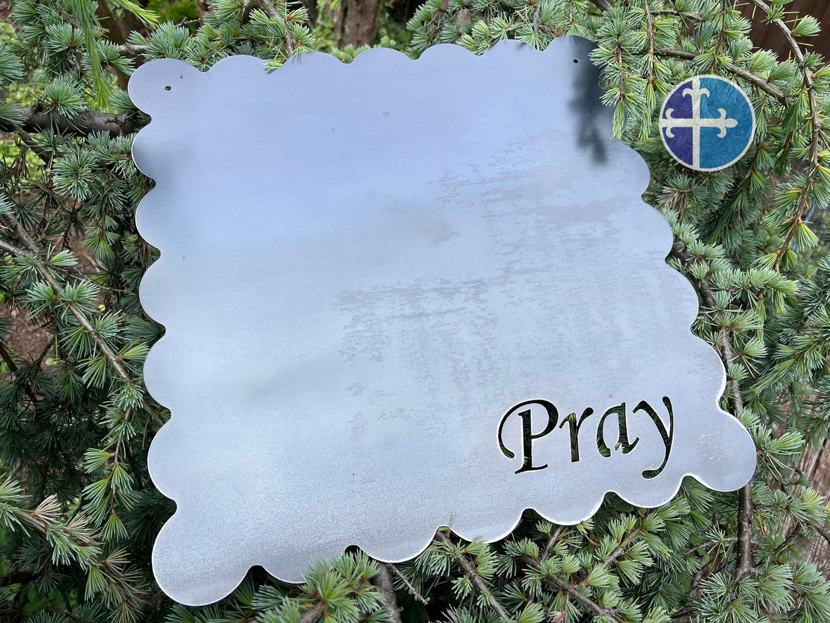 Overhead view of a raw steel magnet board with scalloped edges and Pray cut into the lower corner.