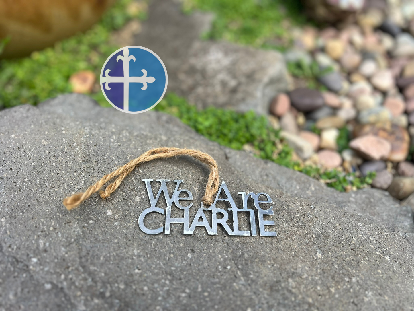 Personalized steel ornament with bold text and twine loop, placed on natural stone.