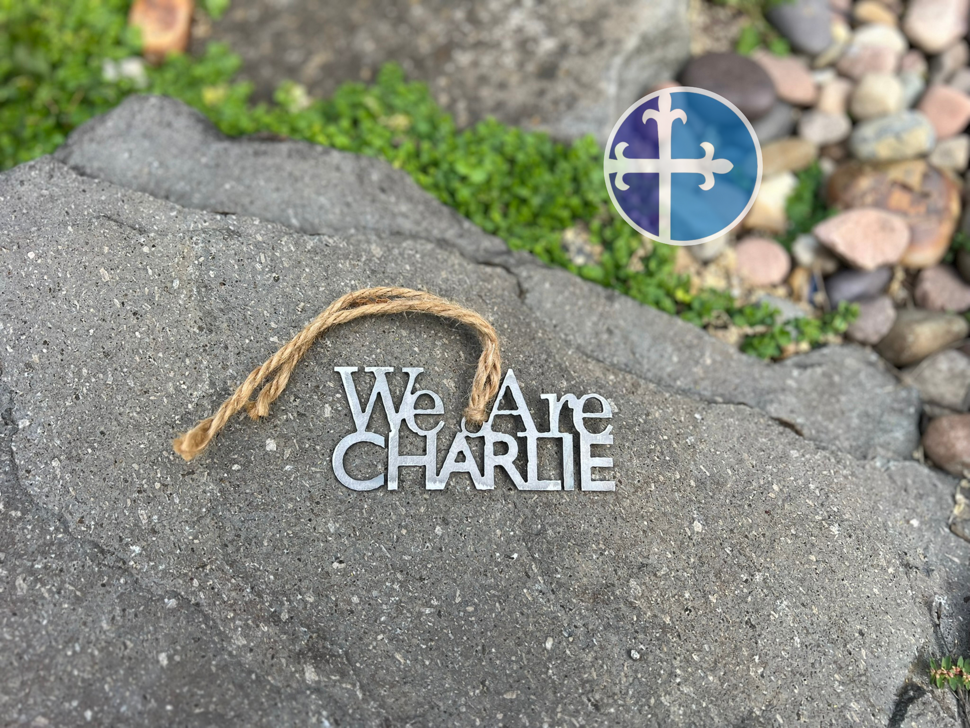 Decorative sign 'We Are CHARLIE' on a rock with a visible brand logo.