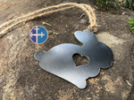 Load image into Gallery viewer, A metal bunny ornament with a heart cutout hanging on a rustic jute string, displayed on a stone background.
